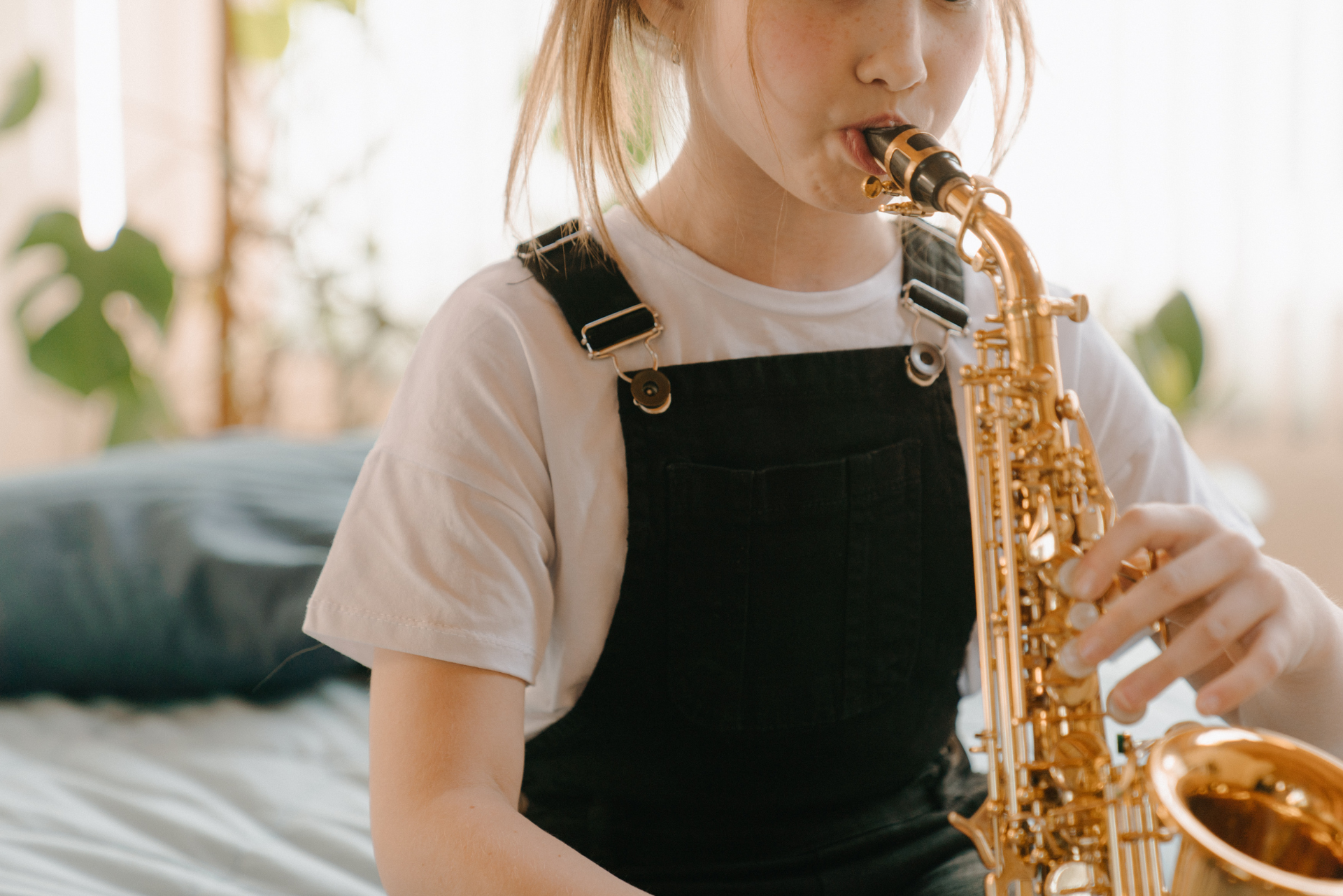 A young girl is playing a saxophone on a bed.