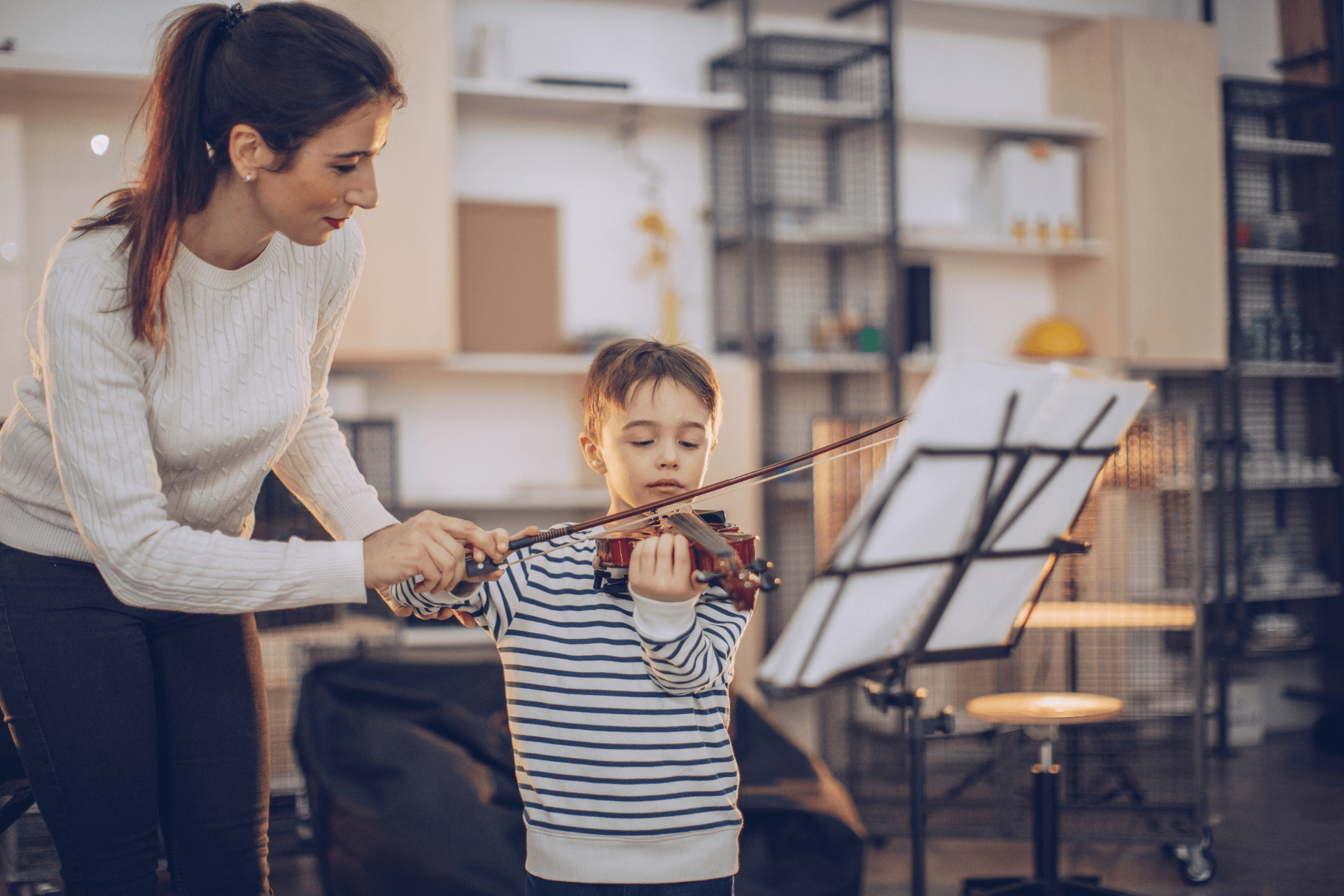 A woman is teaching a young boy how to play a violin.