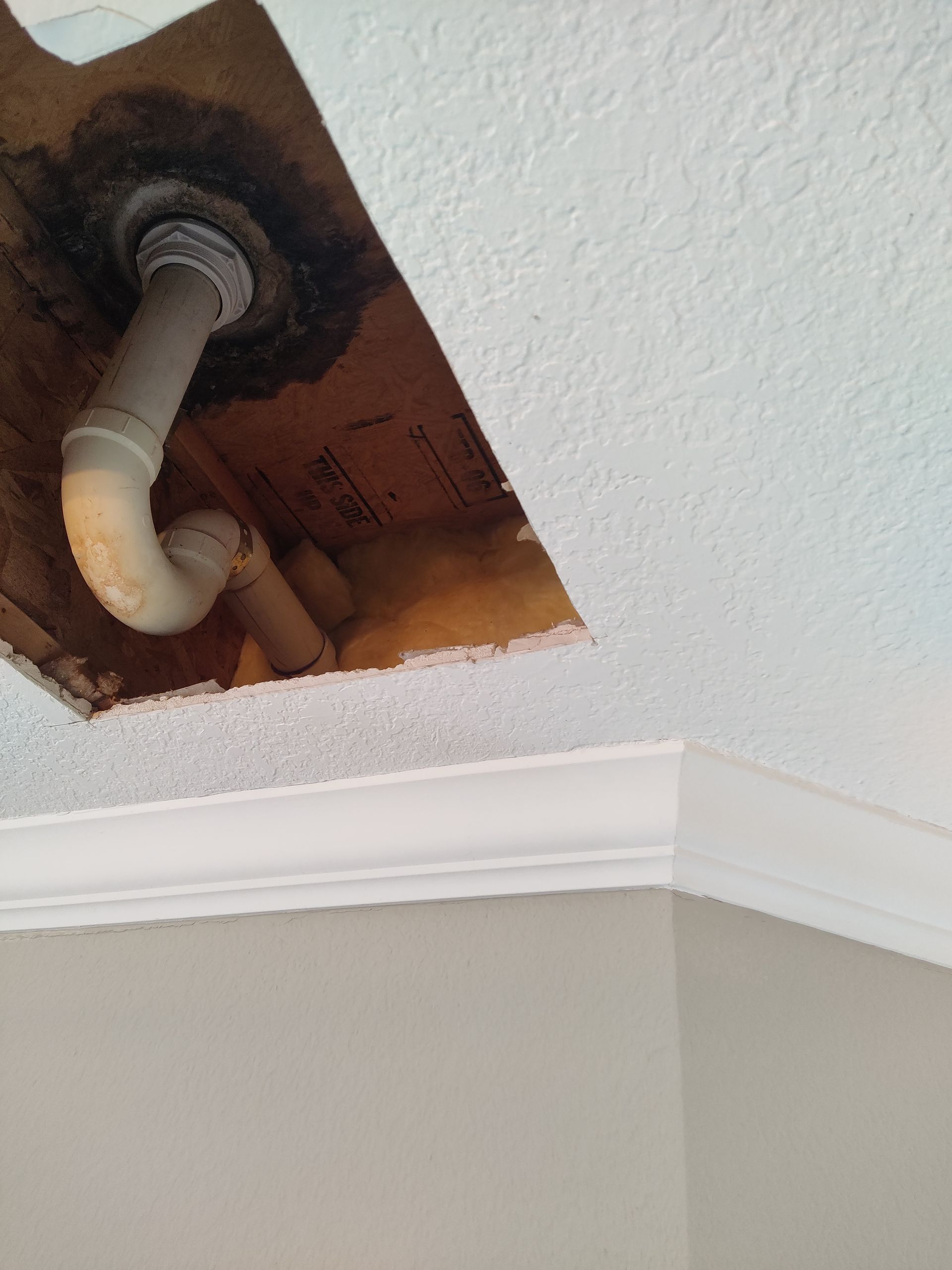 A rectangular hole in a white ceiling reveals the interior joists and a section of PVC plumbing pipe.