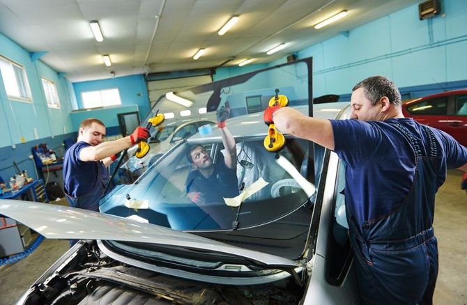 Two men are installing a windshield on a car in a garage.