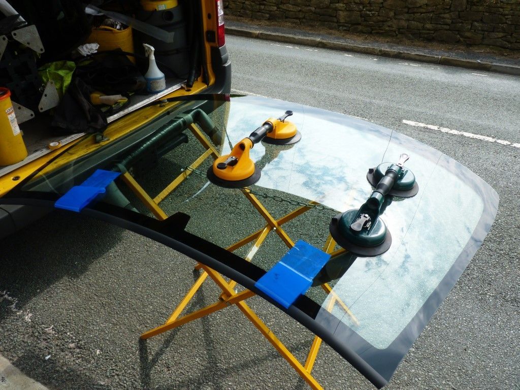 A windshield is being installed on a stand in front of a yellow van.