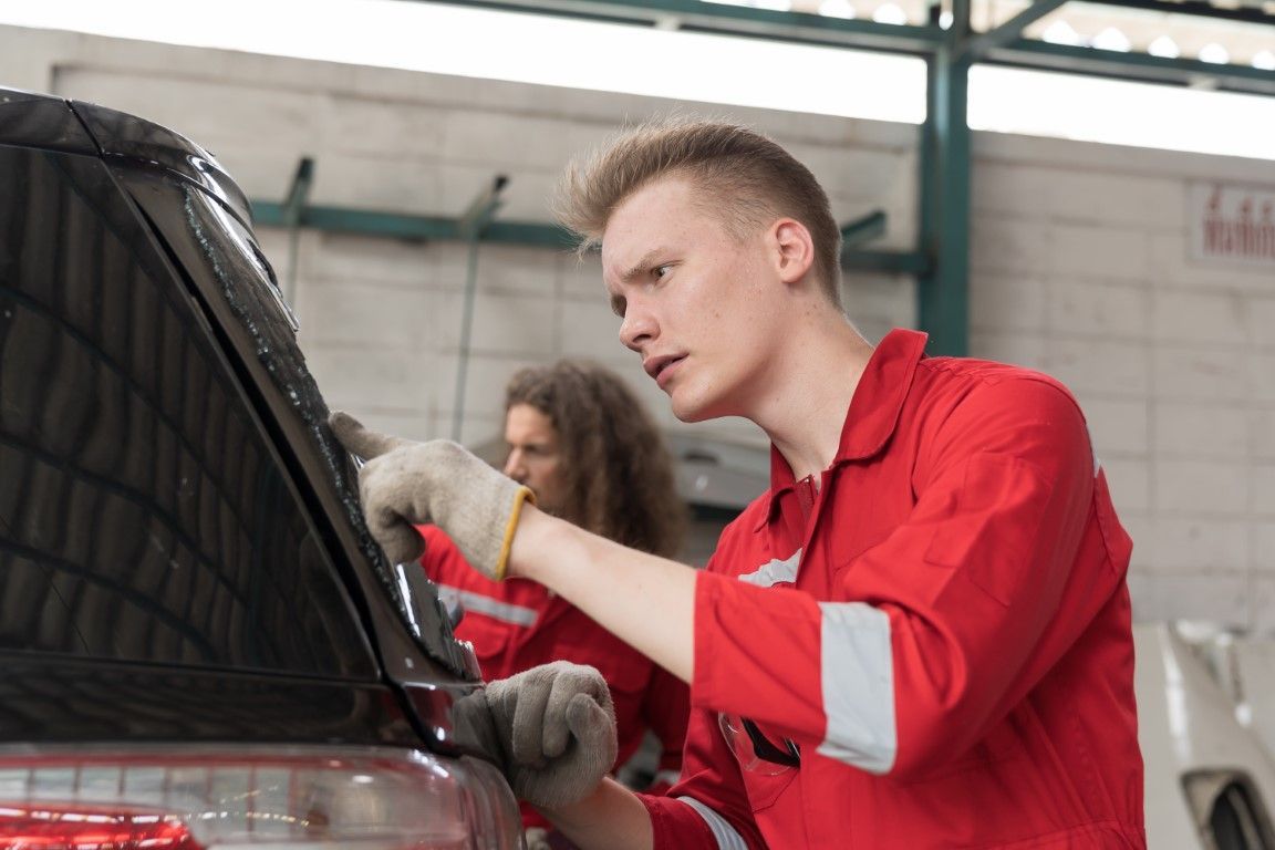 A man in a red uniform is working on a car in a garage.