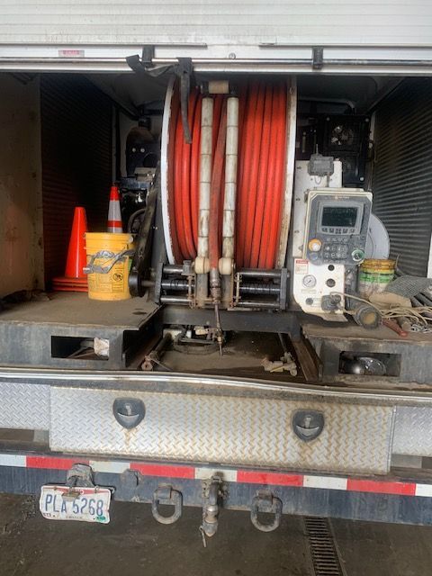 Rear view of a truck's open bed with a large red hose reel, control panel, and storage compartments, parked in a garage.