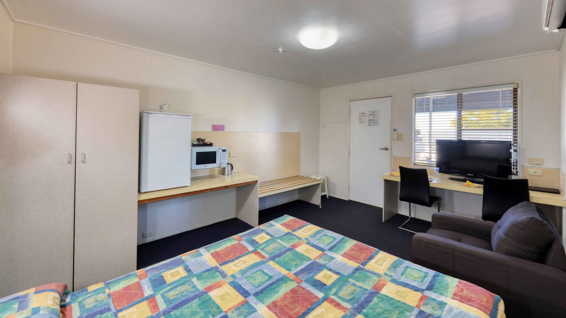 A hotel room with a bed , chair , desk and microwave.