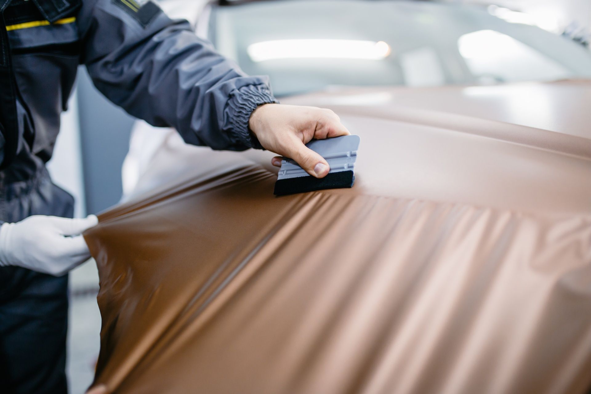 A man is wrapping a car in brown vinyl.