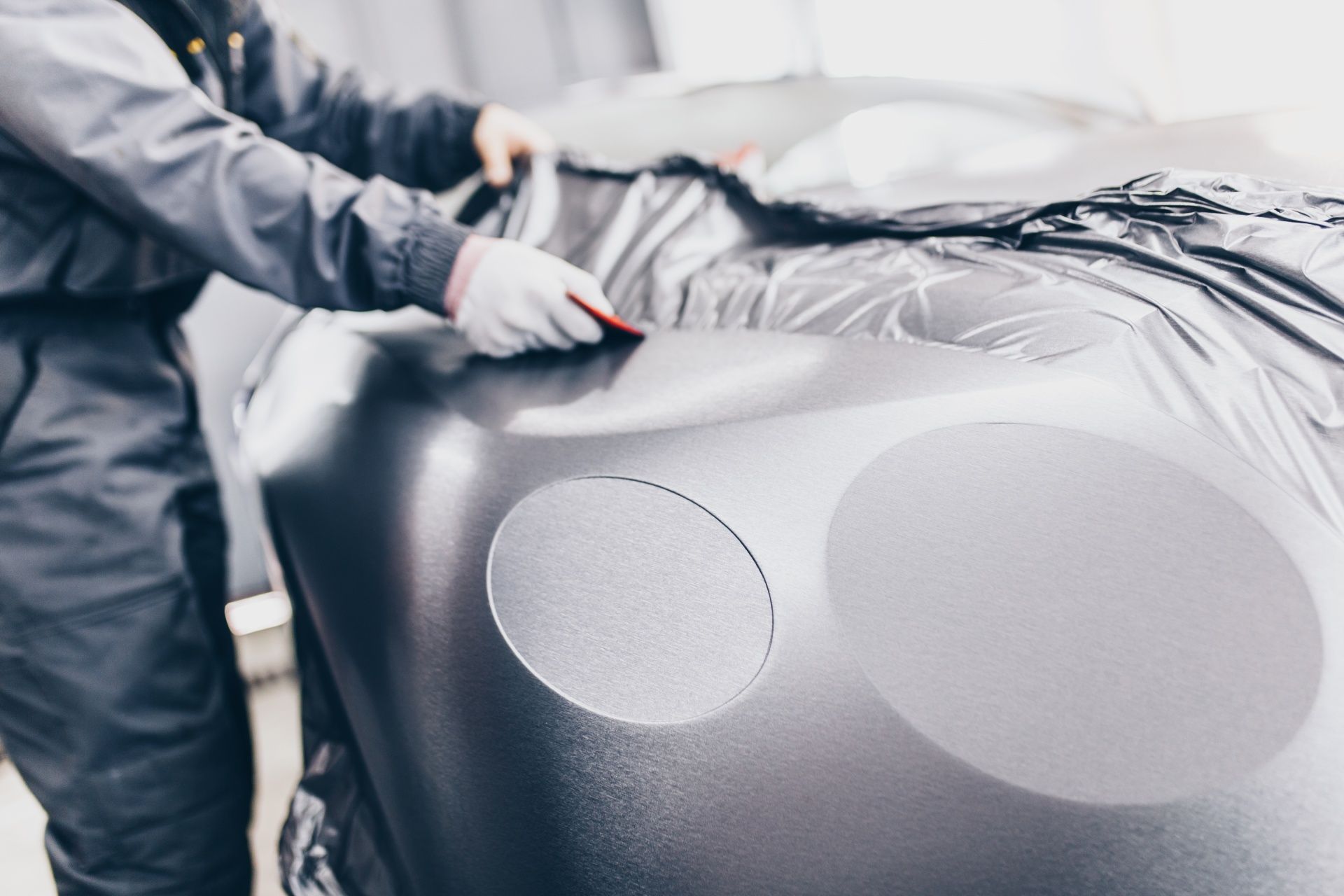 A man is wrapping a car in black vinyl.