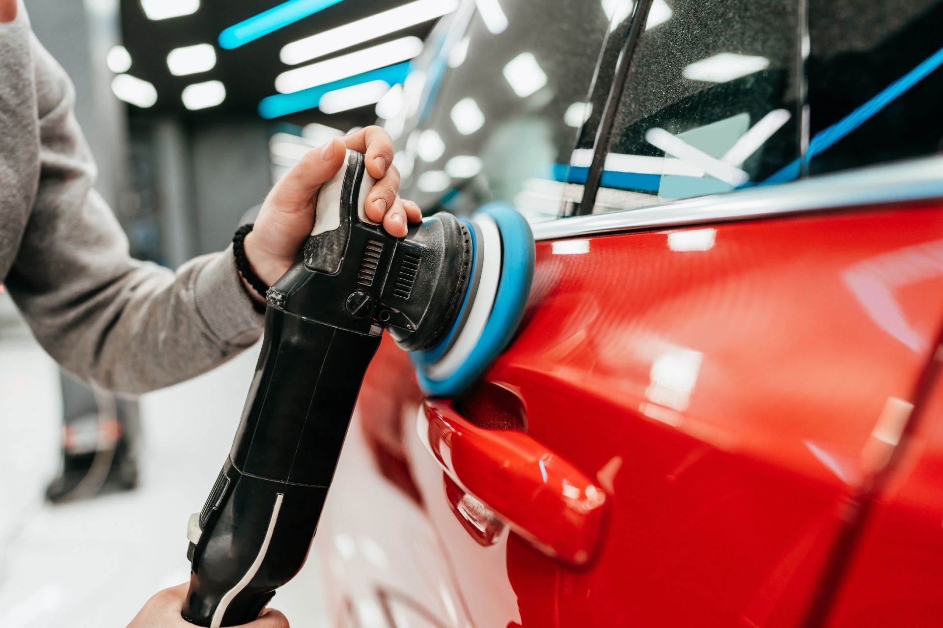 A person is polishing a red car with a machine.