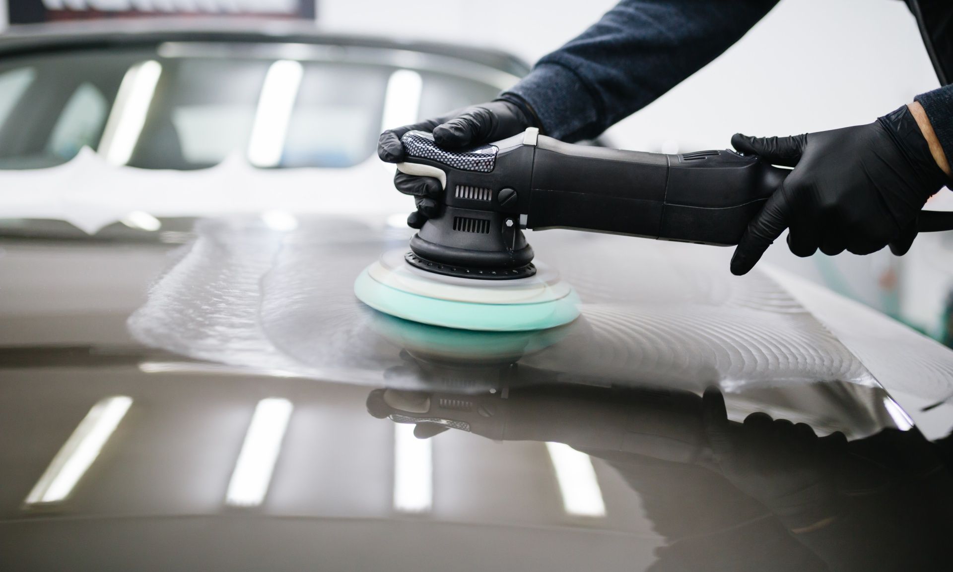 A man is polishing the hood of a car with a machine.