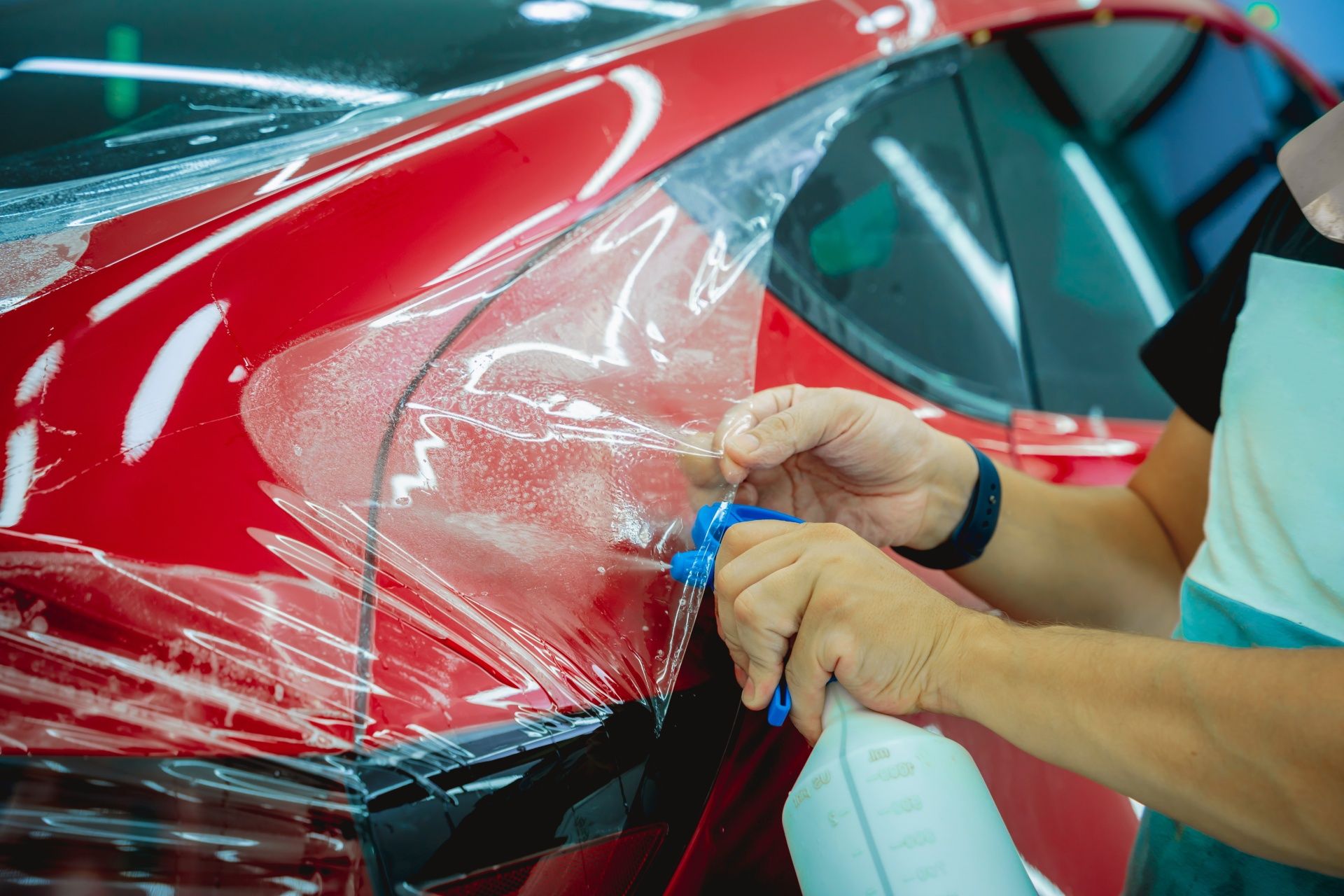 A man is applying a protective film to a red car.