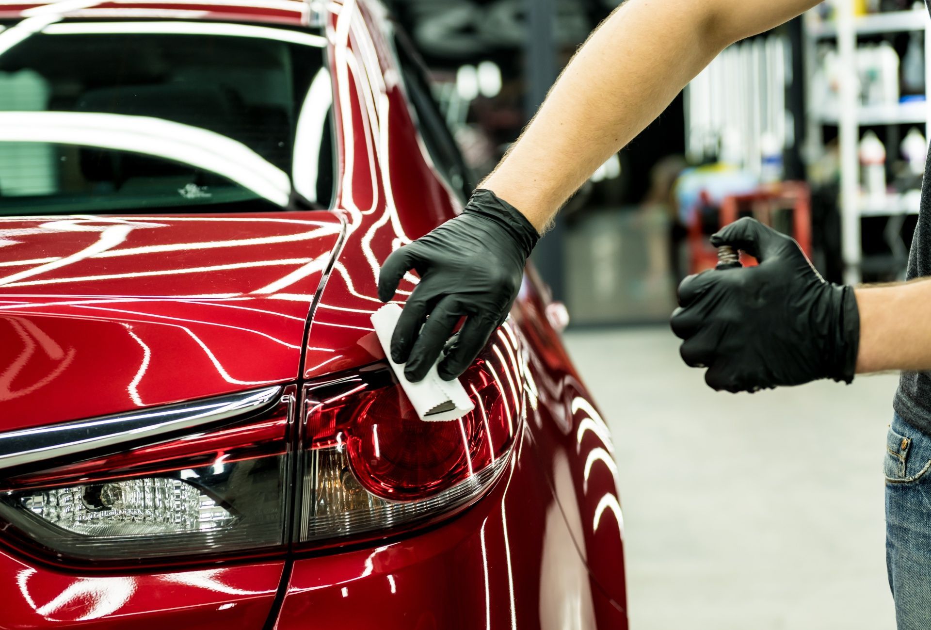 A person wearing black gloves is polishing a red car.