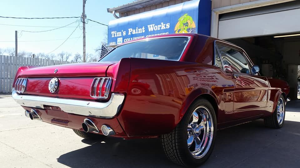 A red mustang is parked in front of a building that says the 's paint works.