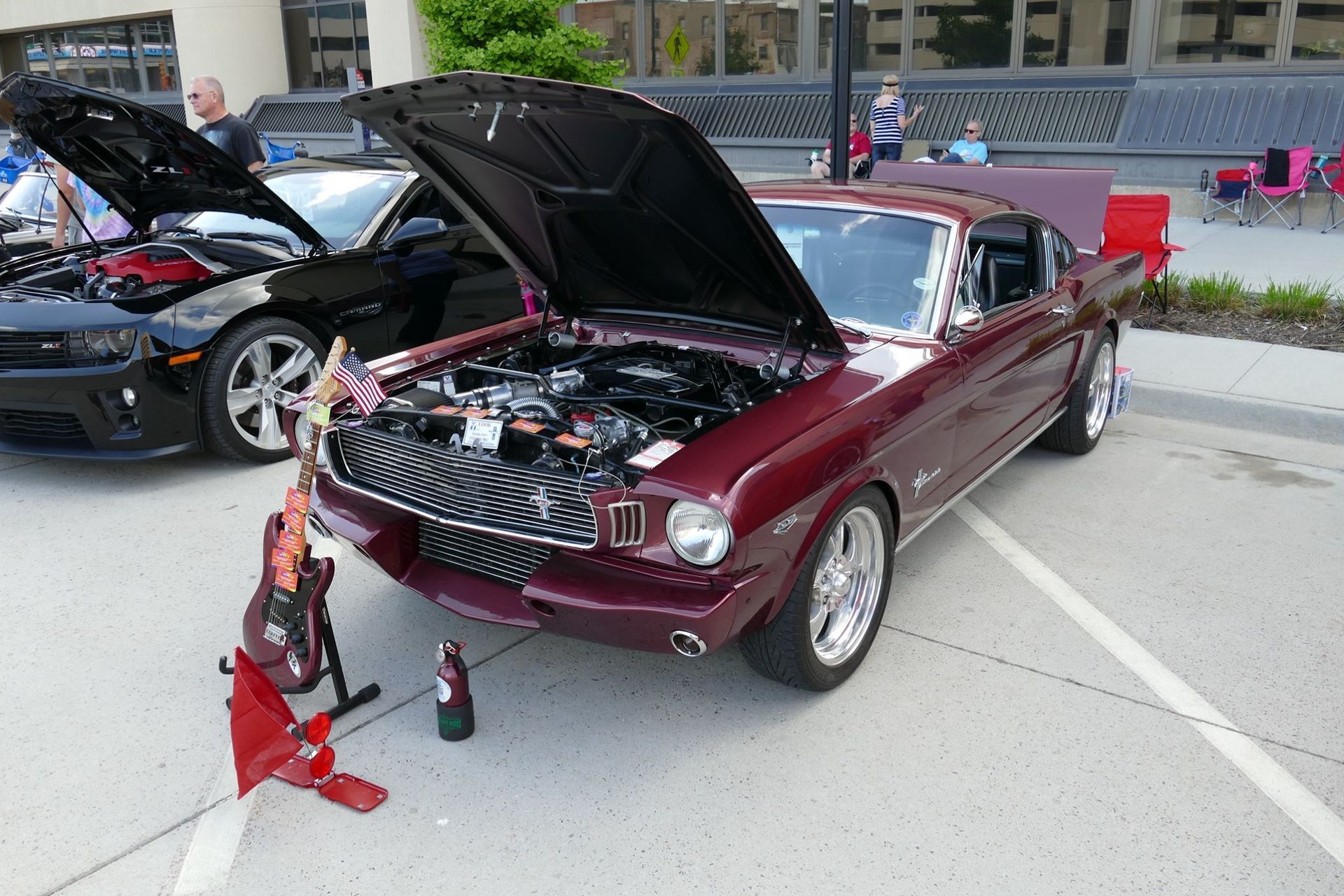 A red mustang with the hood up is parked in a parking lot