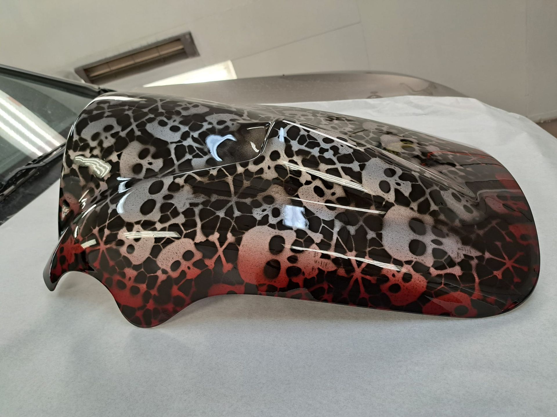 A motorcycle fender with skulls painted on it is sitting on a table.