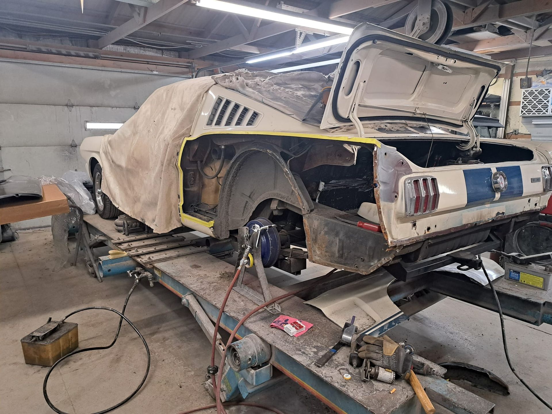 A car is being restored in a garage with the hood open.