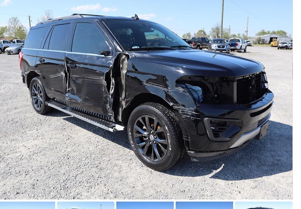 A black suv with a damaged side is parked in a parking lot.