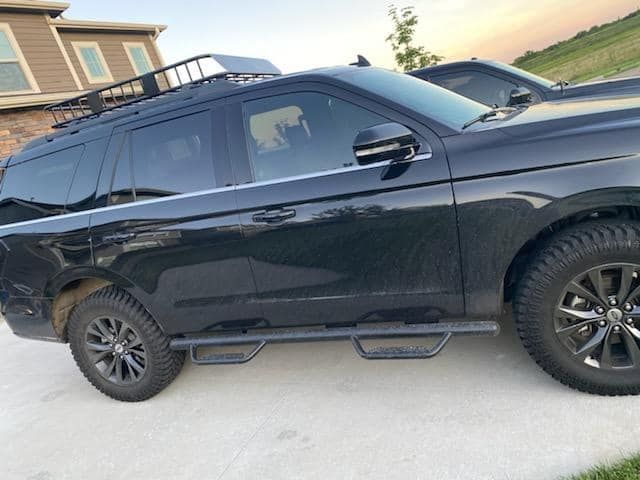 A black suv with a roof rack is parked in a driveway