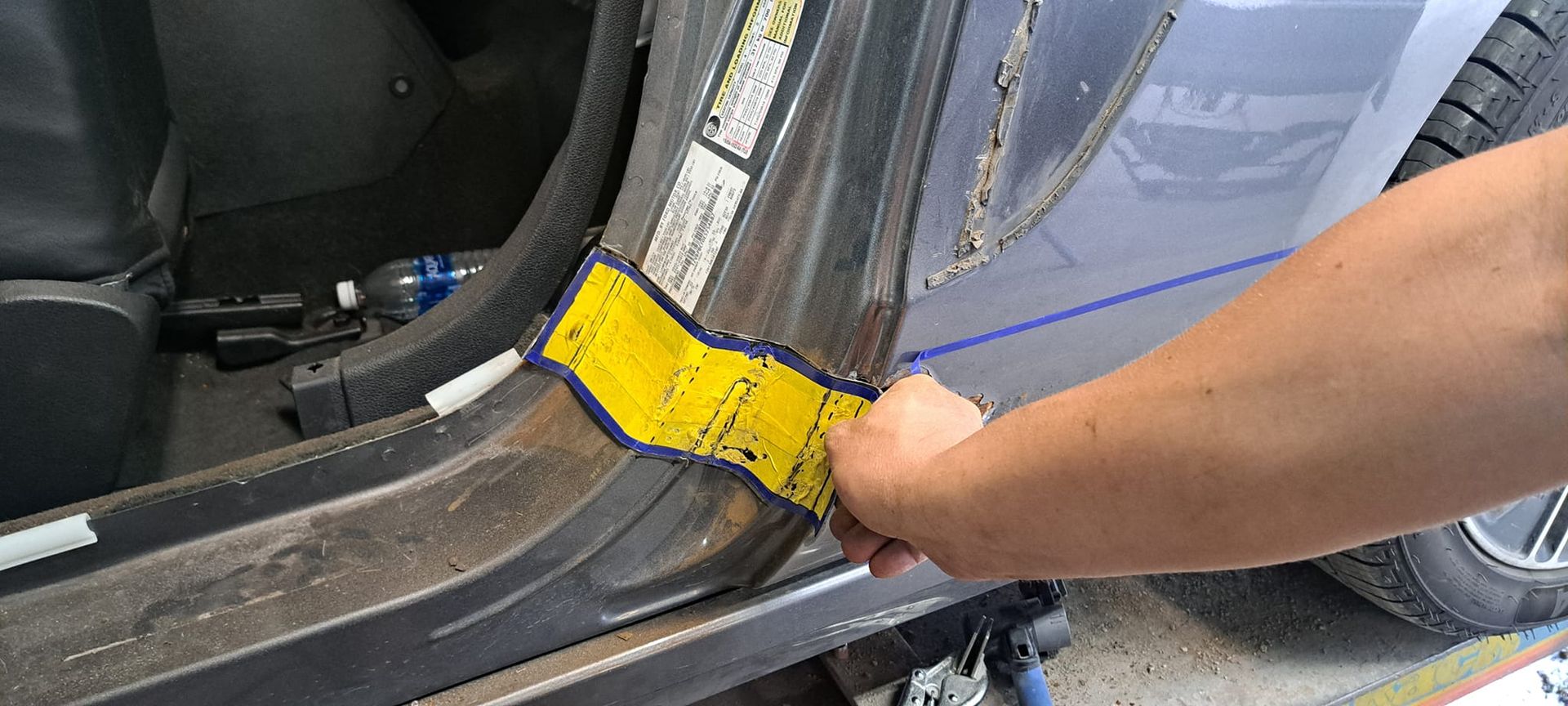 A person is measuring a piece of metal on the side of a car.