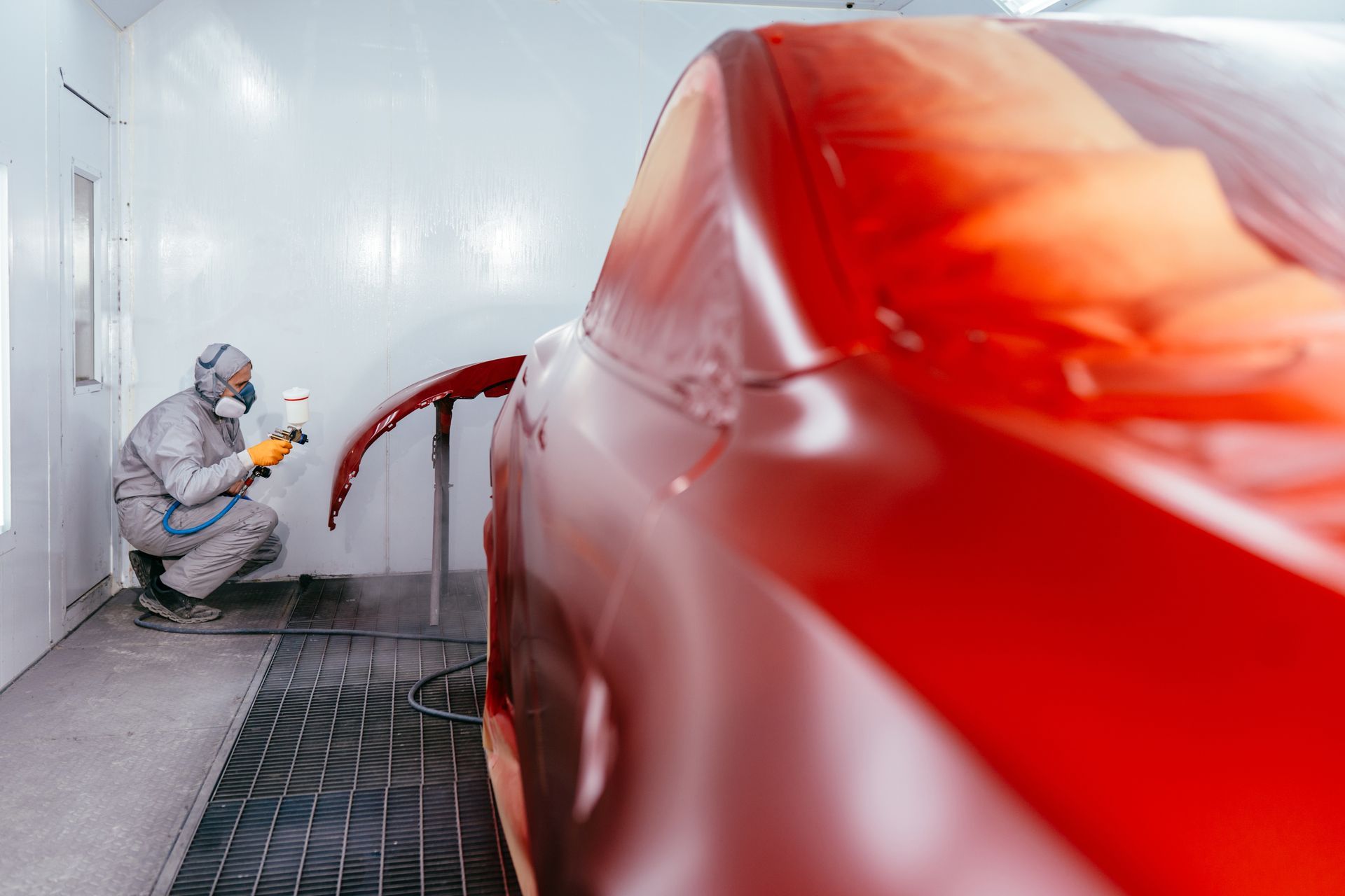 A man is painting a red car in a paint booth.