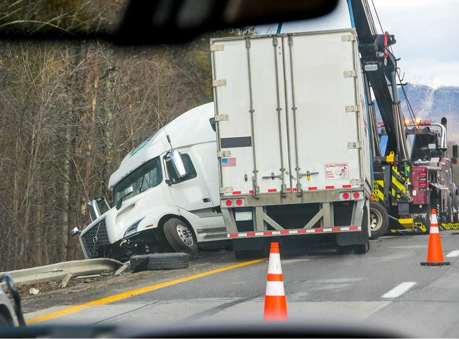 A semi truck is being towed down the road by a tow truck.