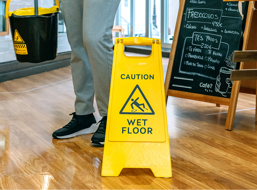 A person is standing next to a yellow wet floor sign.
