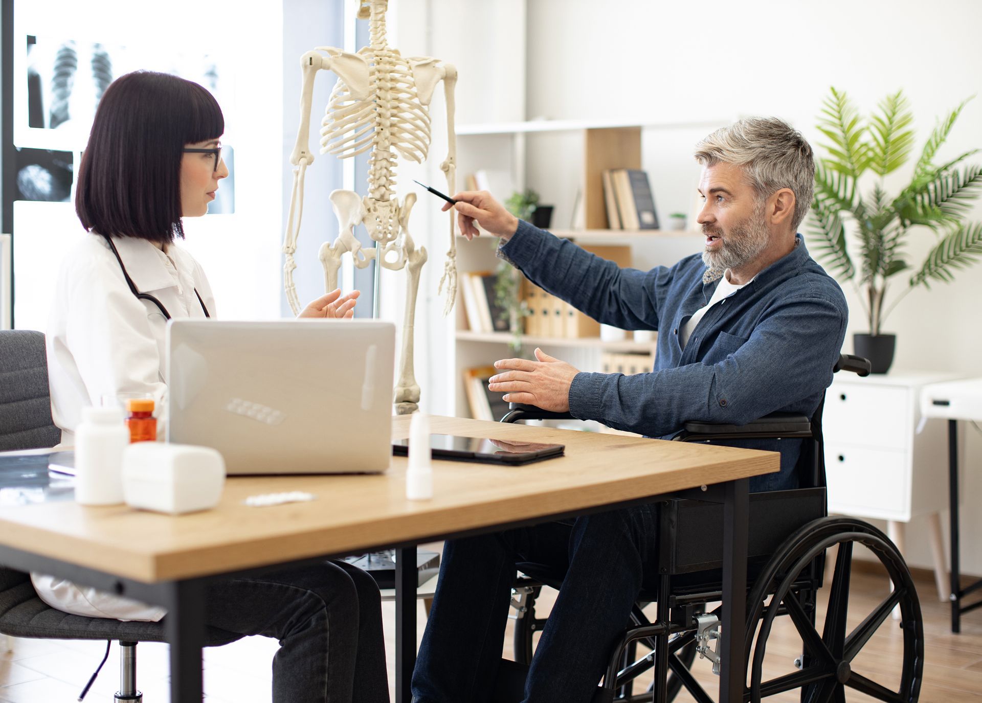 A man in a wheelchair is sitting at a table talking to a doctor.