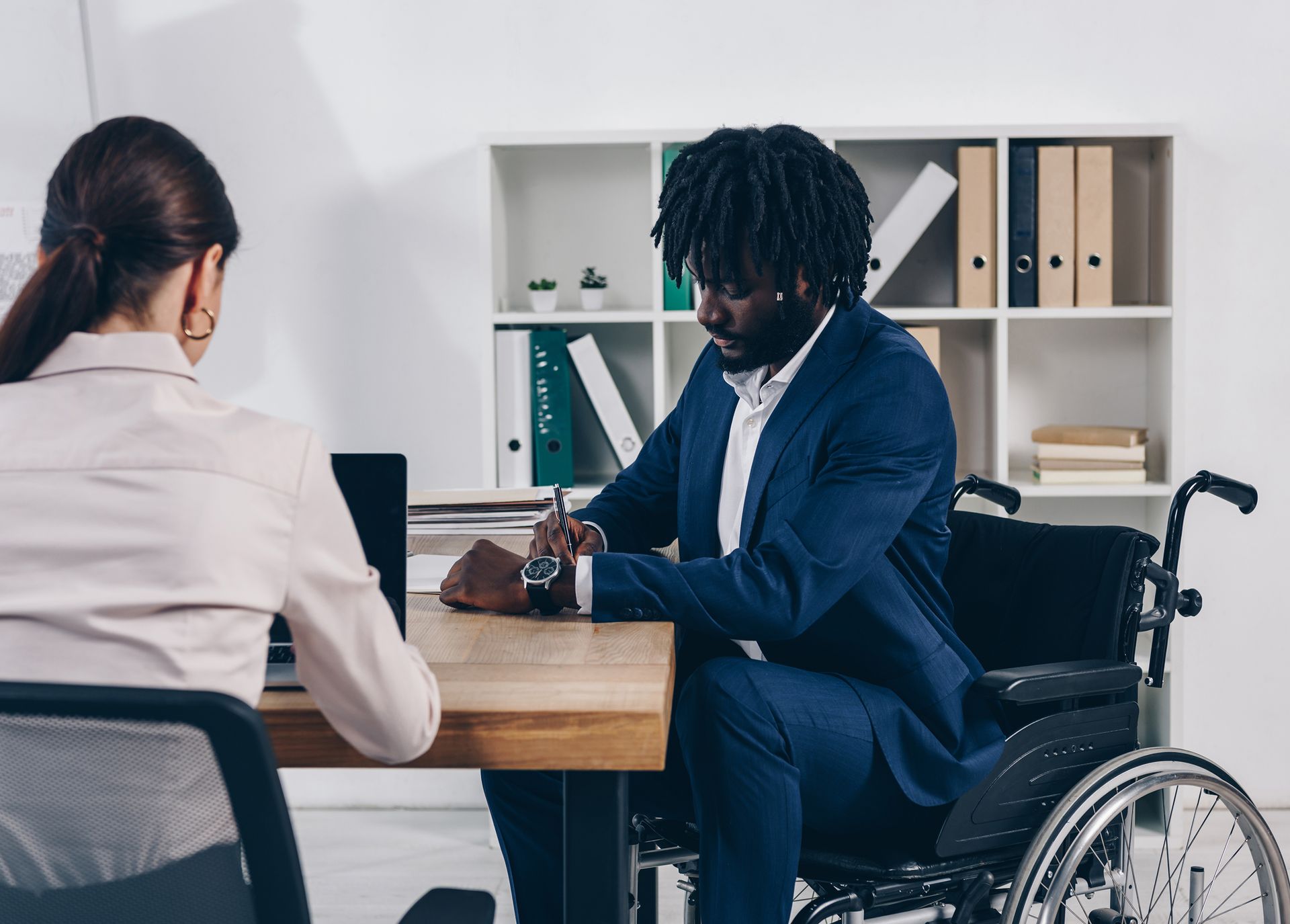 A man in a wheelchair is sitting at a desk with a woman.