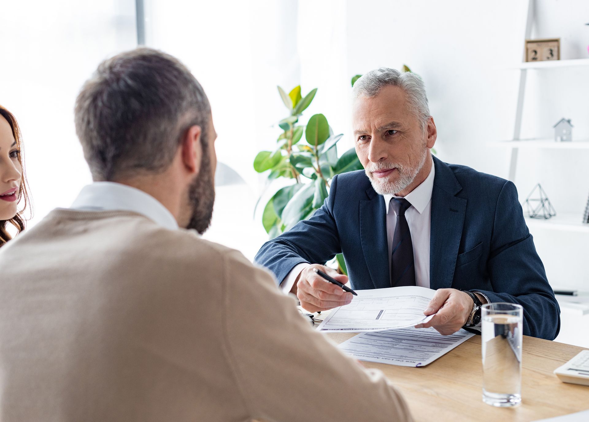 A man in a suit and tie is sitting at a table talking to a man and woman.
