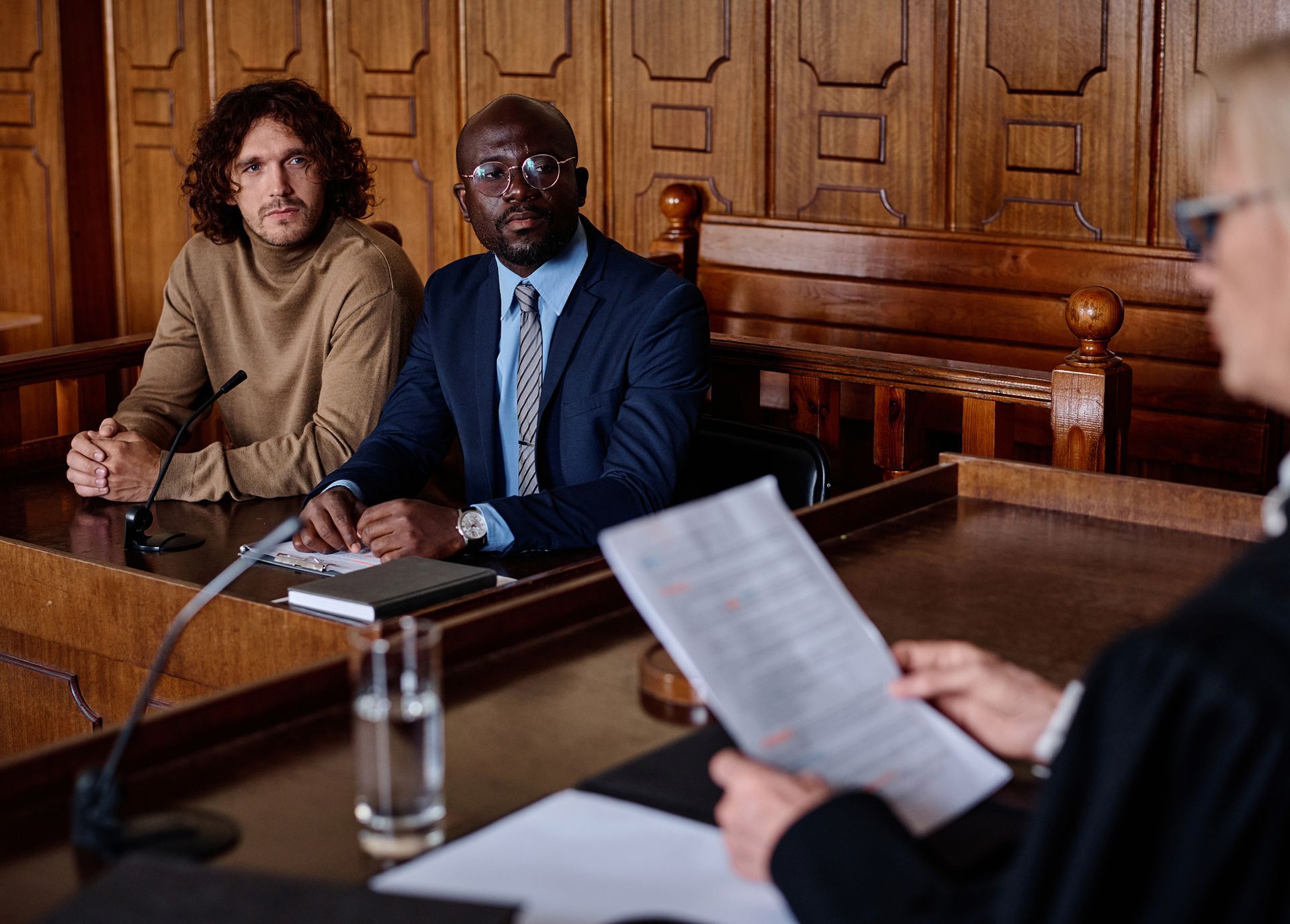 Two men are sitting at a table in front of a judge in a courtroom.