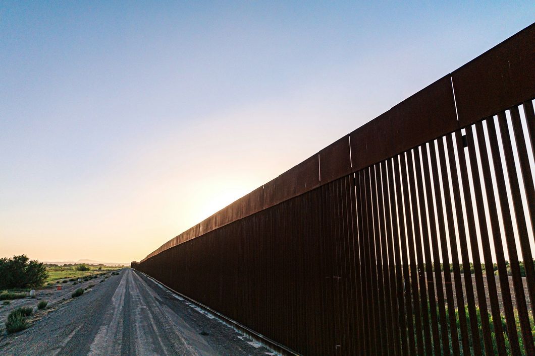 A fence along a dirt road with a sunset in the background.