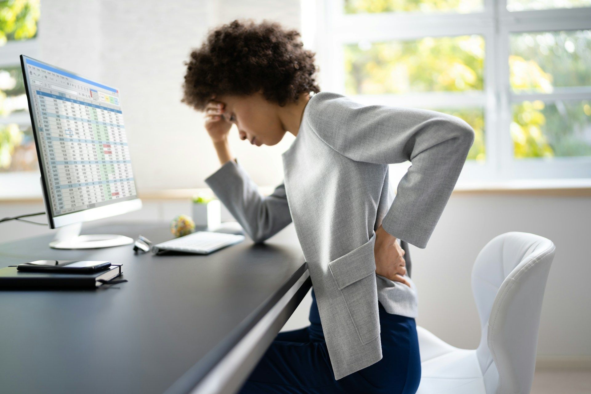 A woman is sitting at a desk with her back in pain.