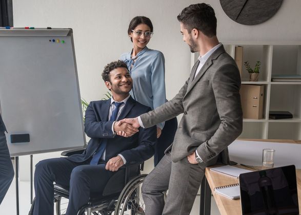 A man in a suit is shaking hands with a man in a wheelchair.