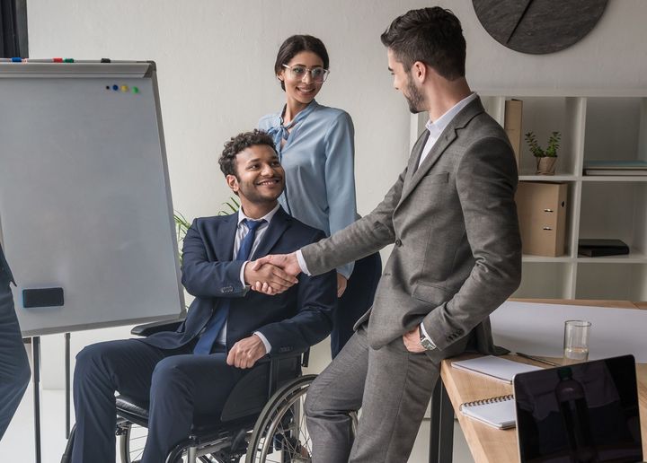A man in a suit is shaking hands with a man in a wheelchair.