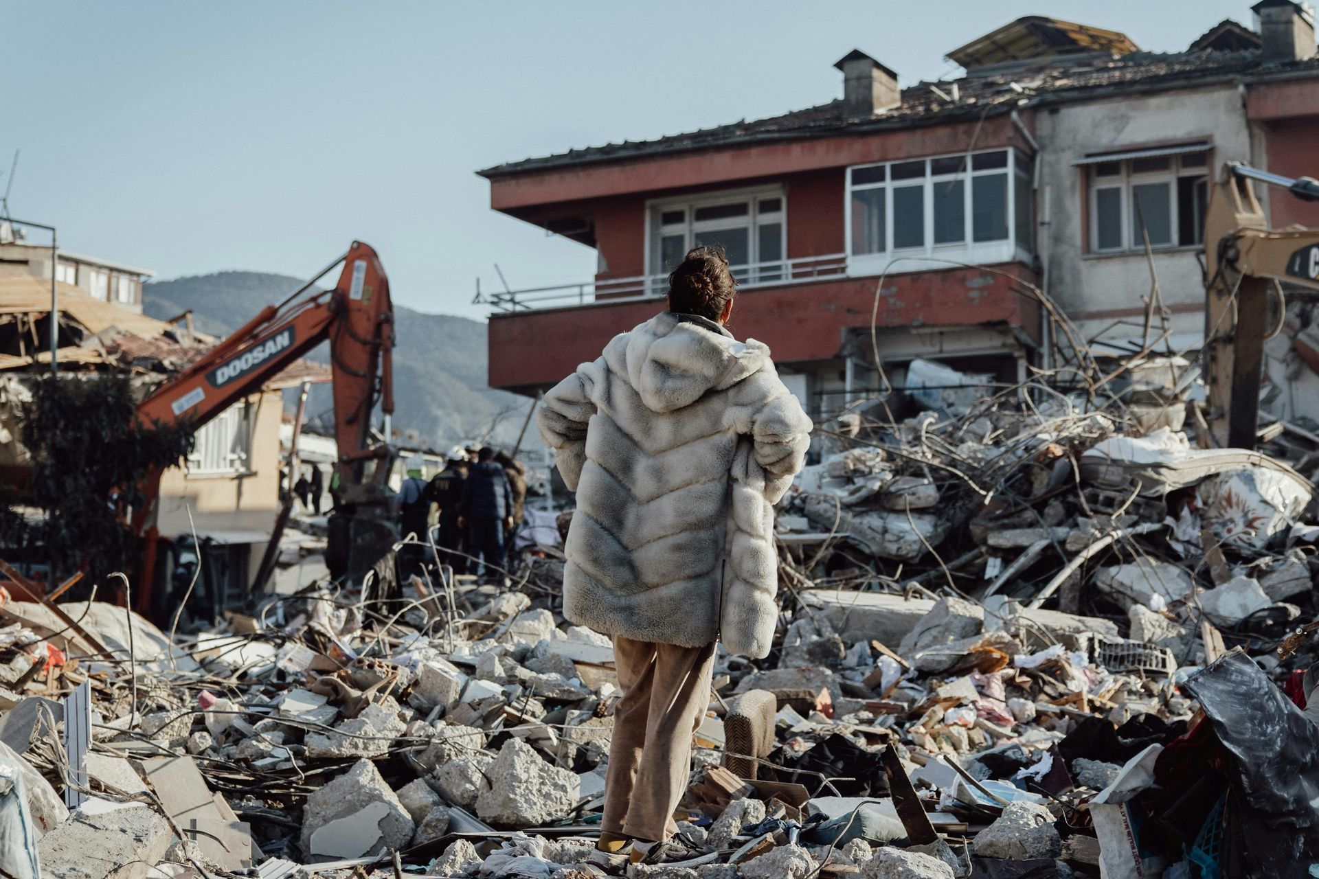 A woman in a fur coat is standing in front of a pile of rubble.