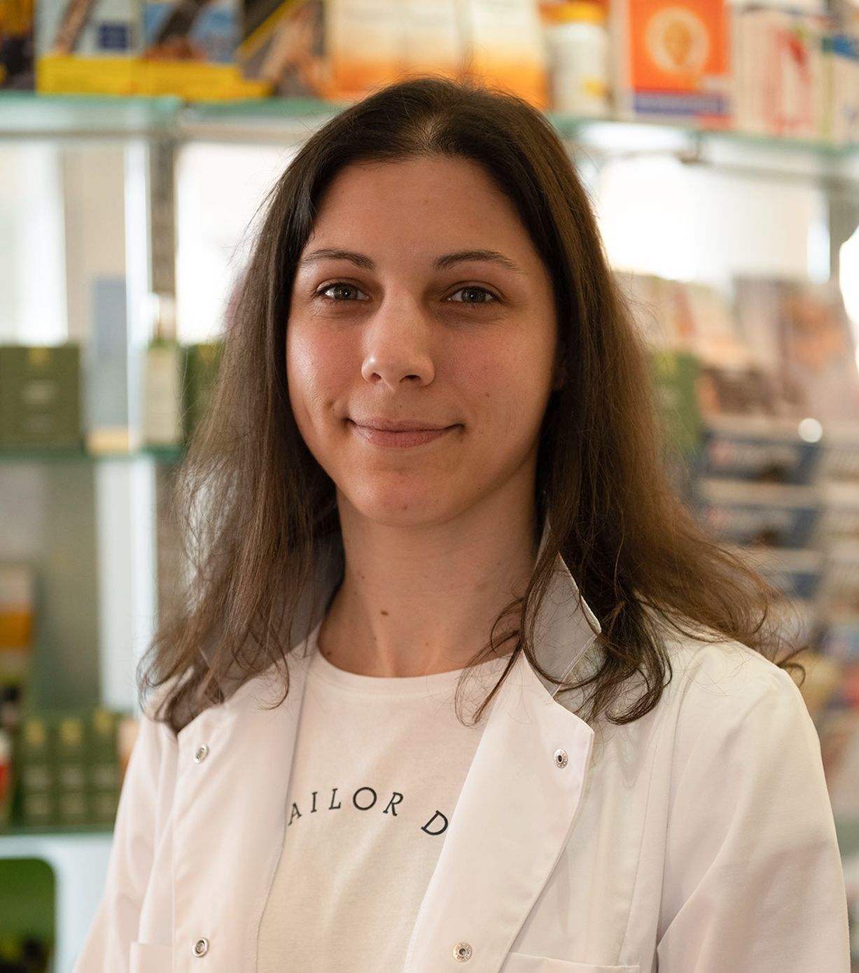 Eine Frau in einem weißen Kittel und einem weißen Hemd steht in einer Apotheke.