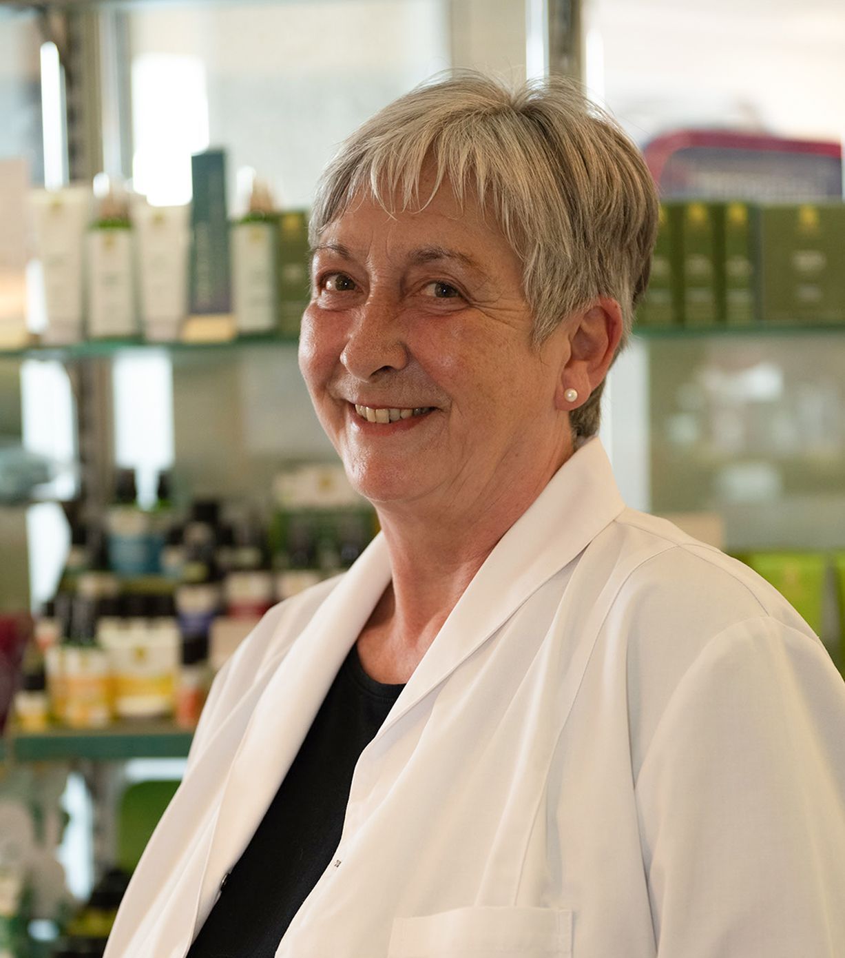 Eine Frau im Laborkittel lächelt vor einem Regal voller Flaschen