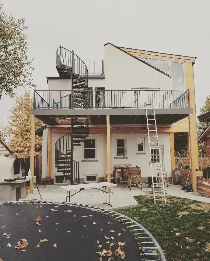 Two-story house with a deck and spiral staircases, under construction. Includes trampoline and construction materials.