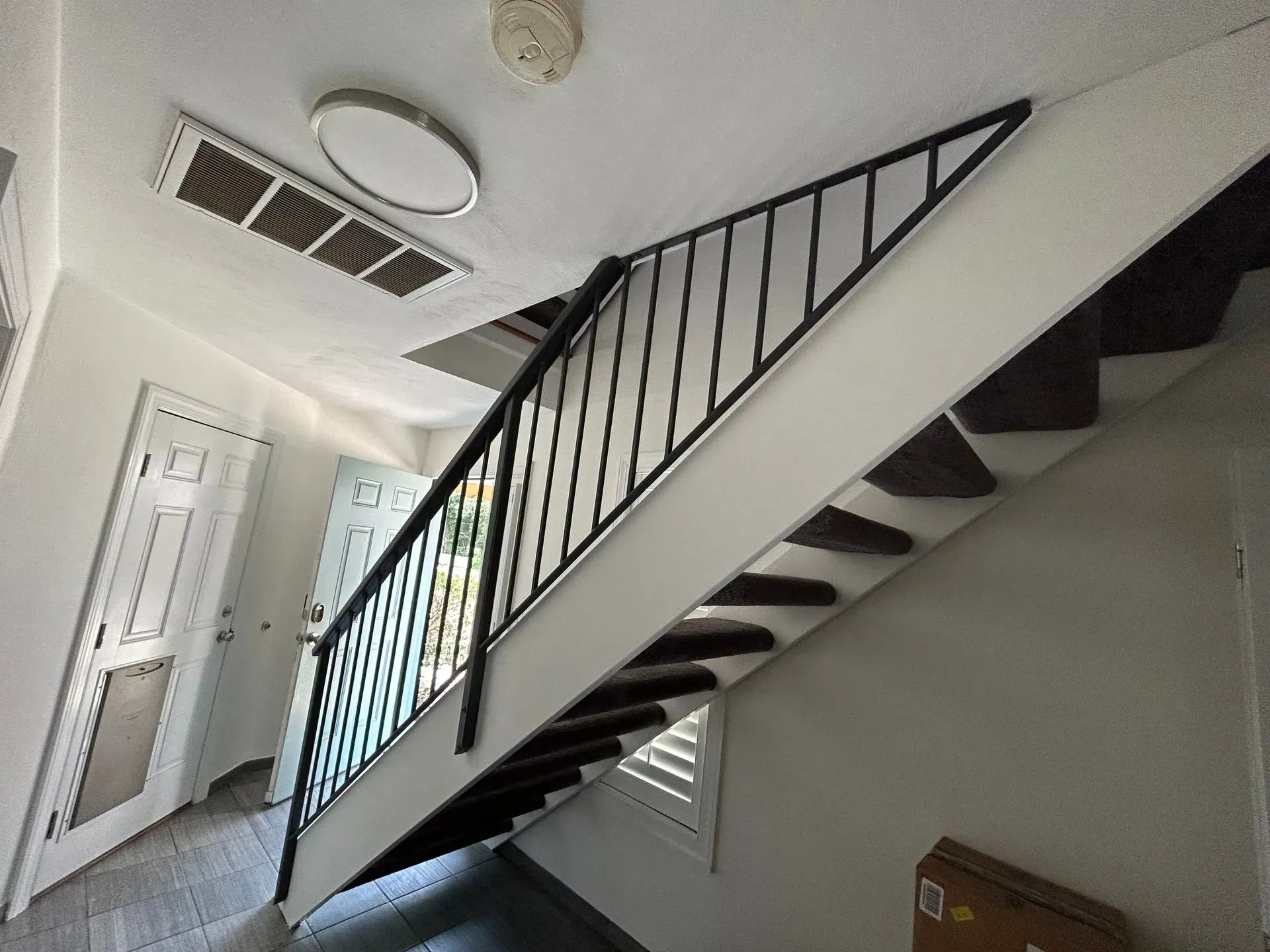 Staircase with black railing and dark-colored carpet leading upwards. The interior has white walls and a door at the bottom.