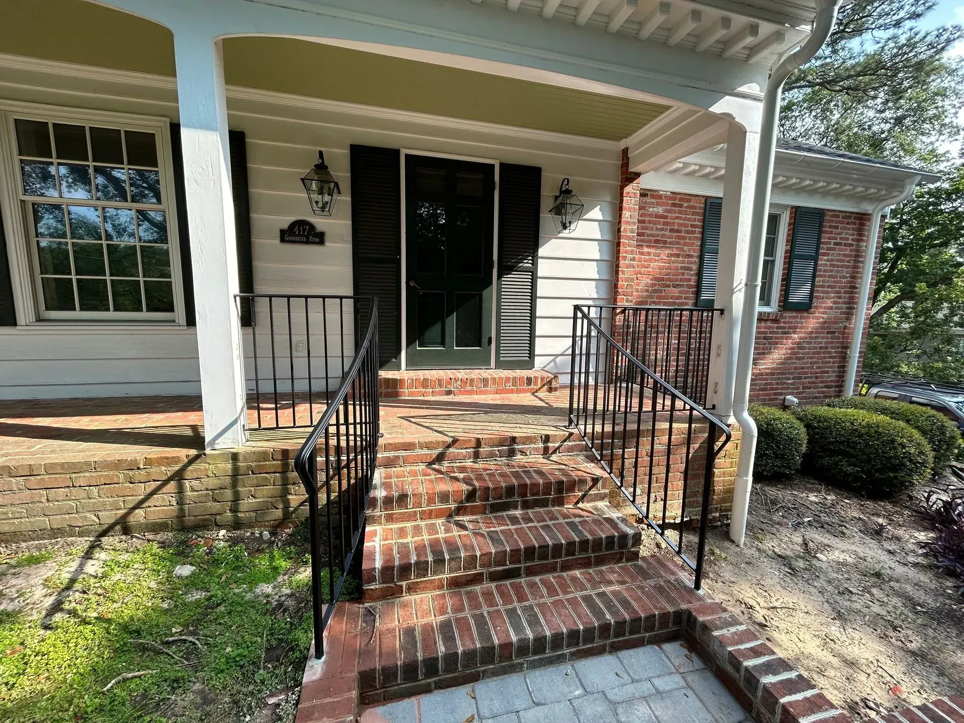A brick-stepped entryway to a white house with black shutters and a black front door. Black metal railings line the steps.
