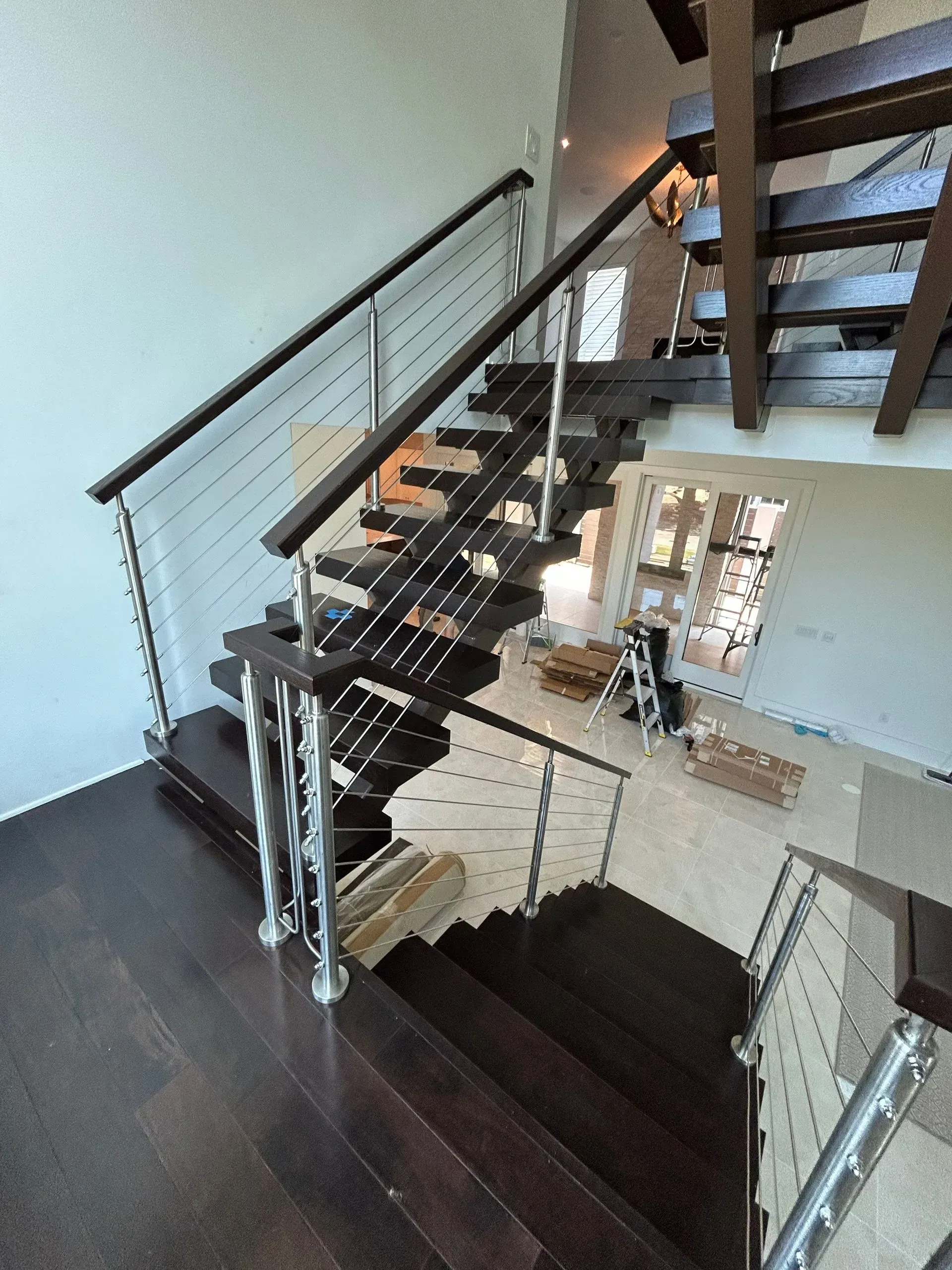 Dark wood staircase with stainless steel railing. Sunlight streams through the windows. 