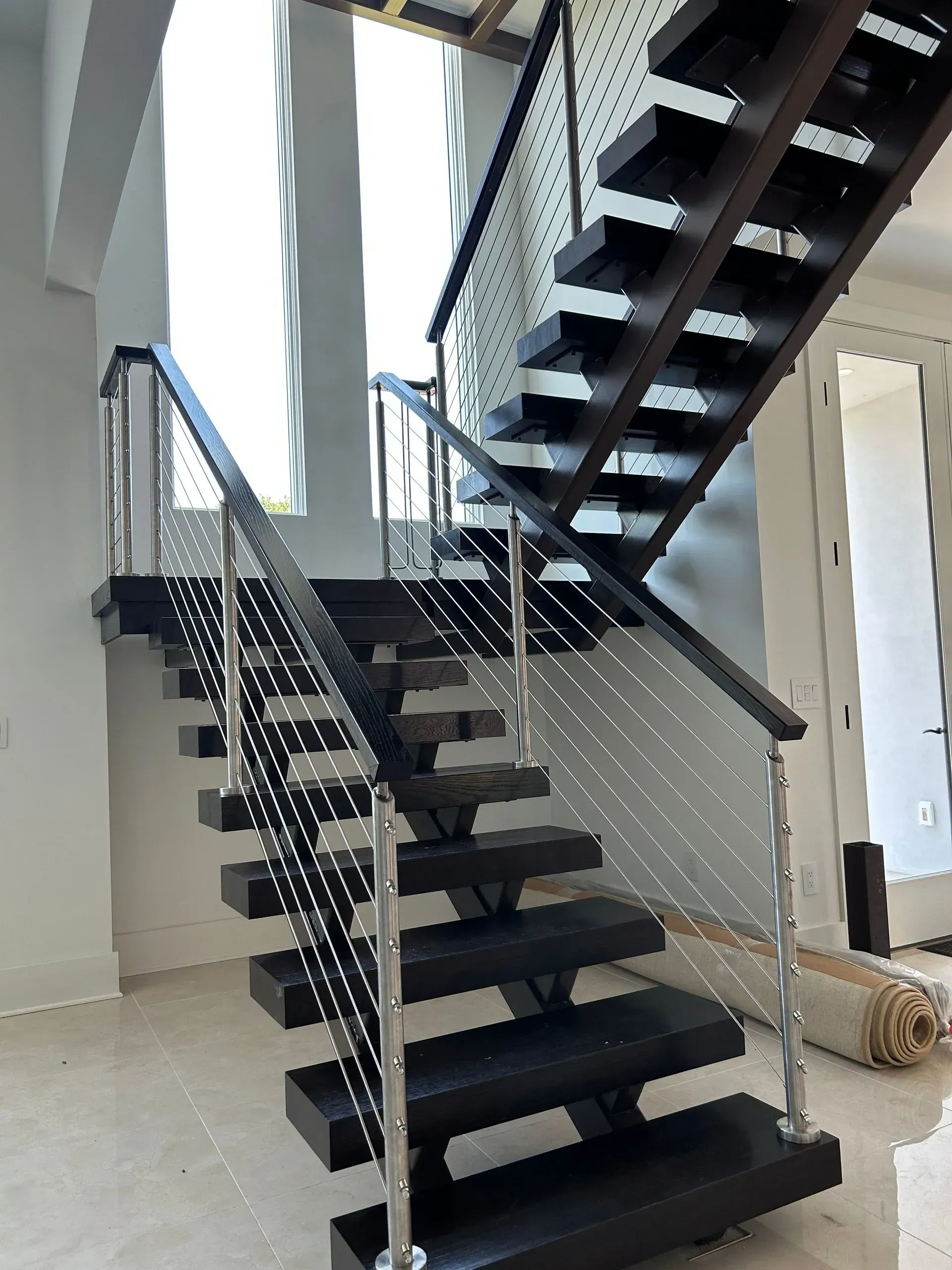 Floating wooden staircase with black treads and stainless steel cable railings. 