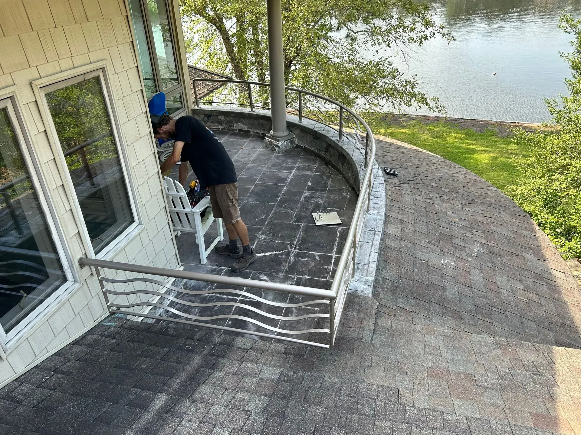 Person working on a curved deck with a decorative metal railing overlooking a lake. 