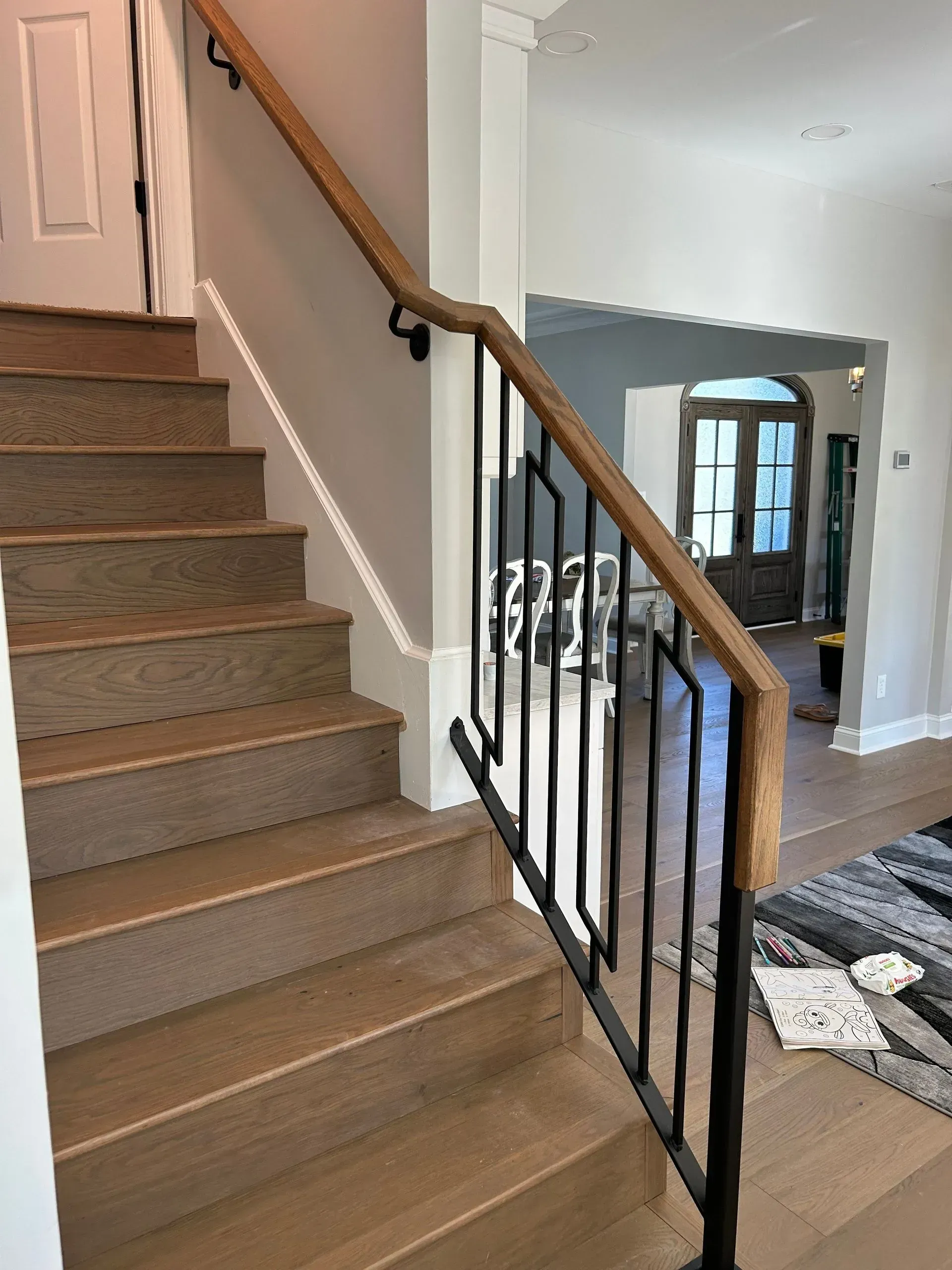 Wooden staircase with dark metal railing, a light-colored wood handrail, and neutral-toned walls. The steps are light brown.