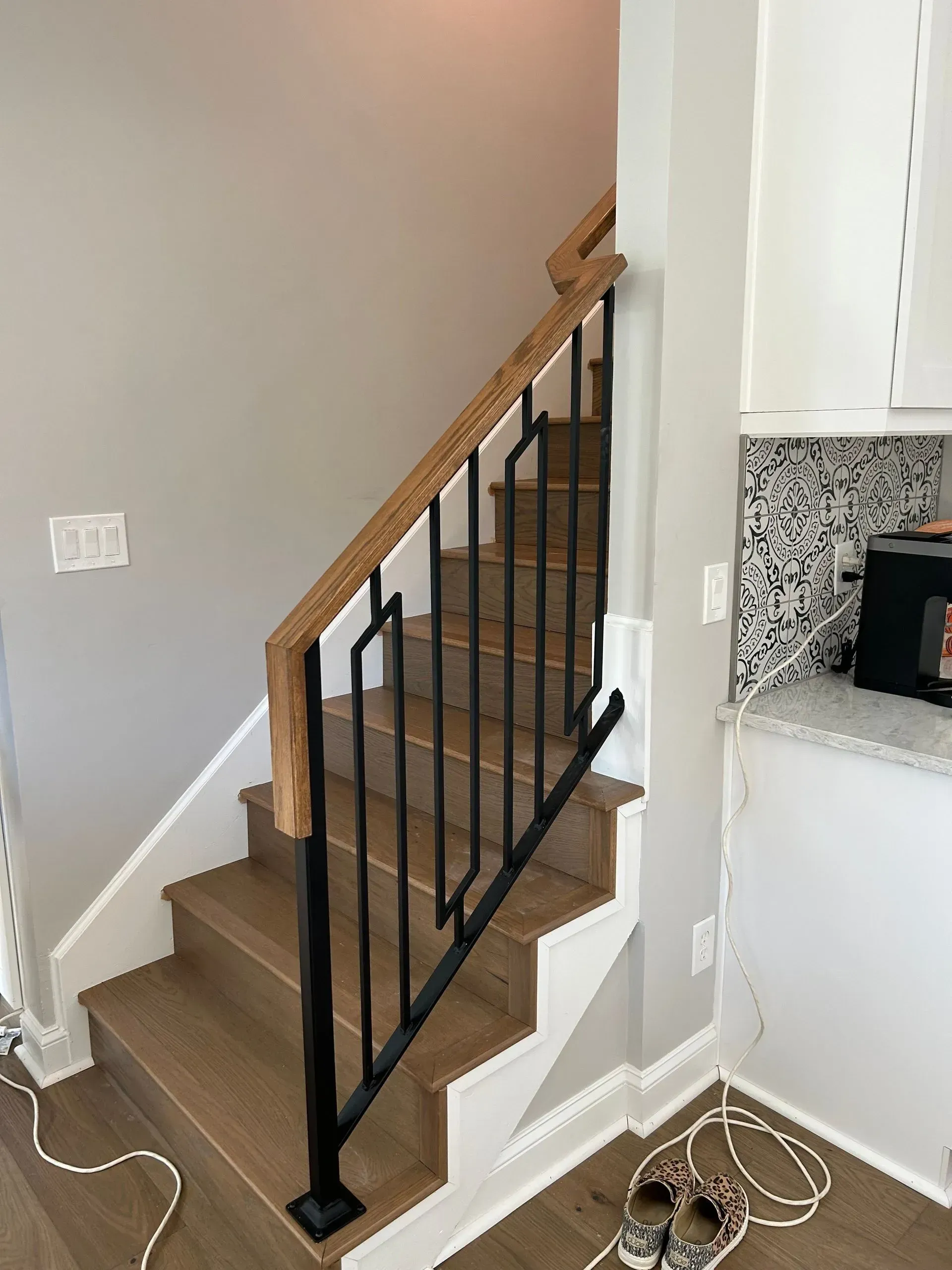Staircase with wood steps and handrail, black metal railing, and light grey walls.  
