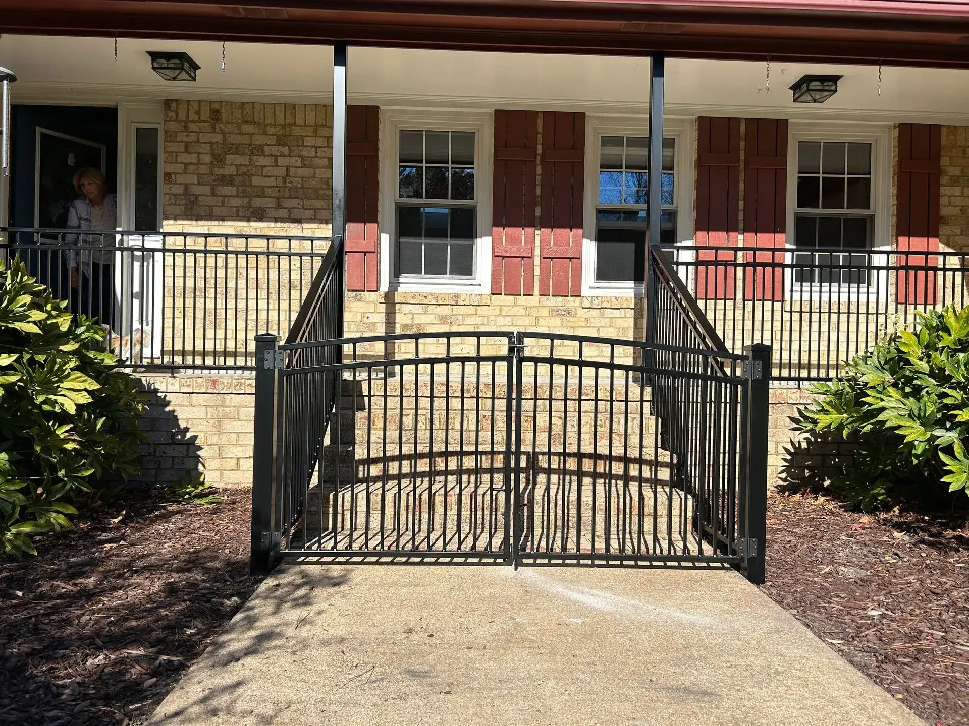 Black iron gate and railing leading up to the entrance of a brick house. 