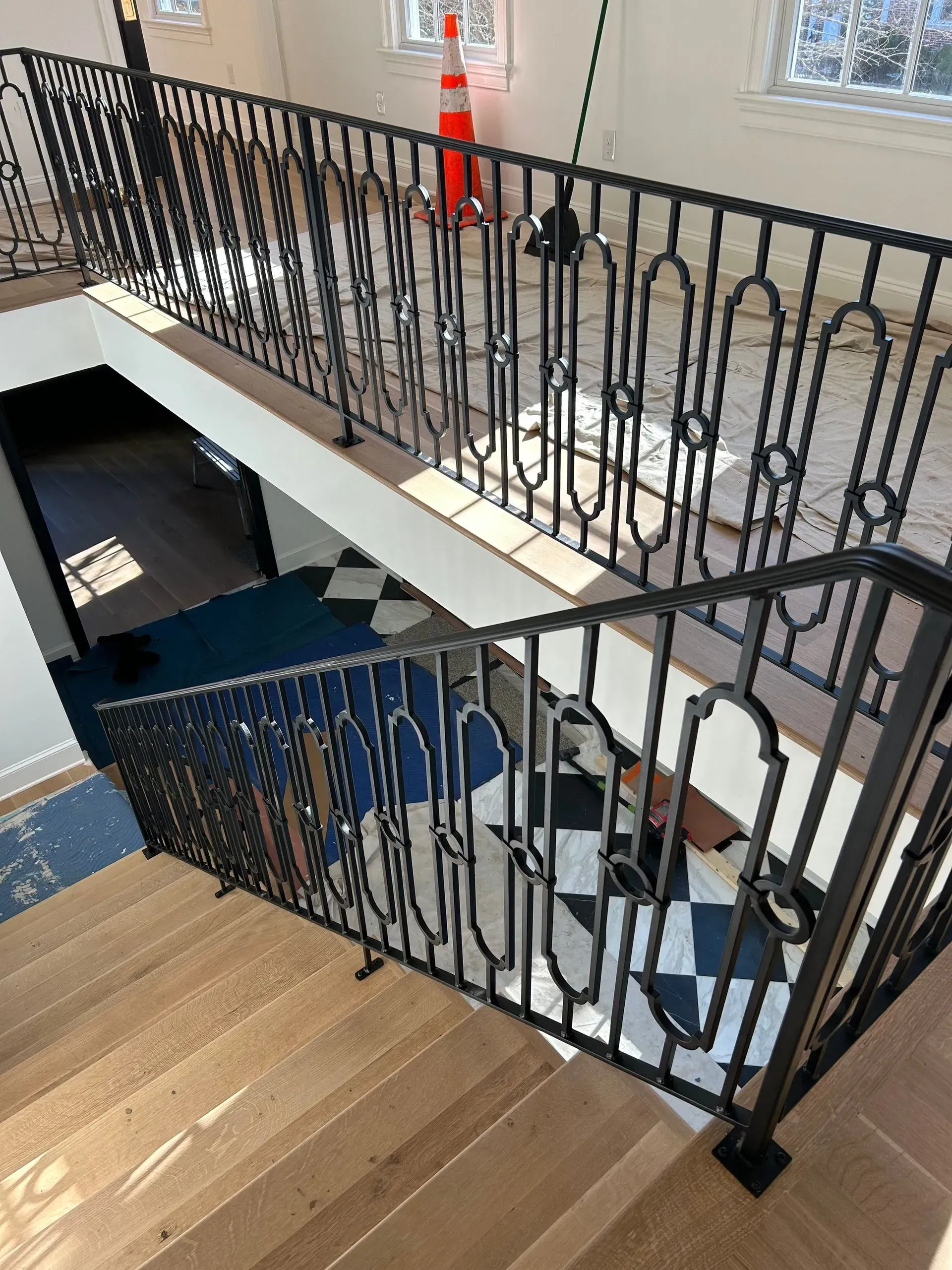 View of a staircase with black wrought iron railings and a black and white checkered floor. The stairs have wooden steps.