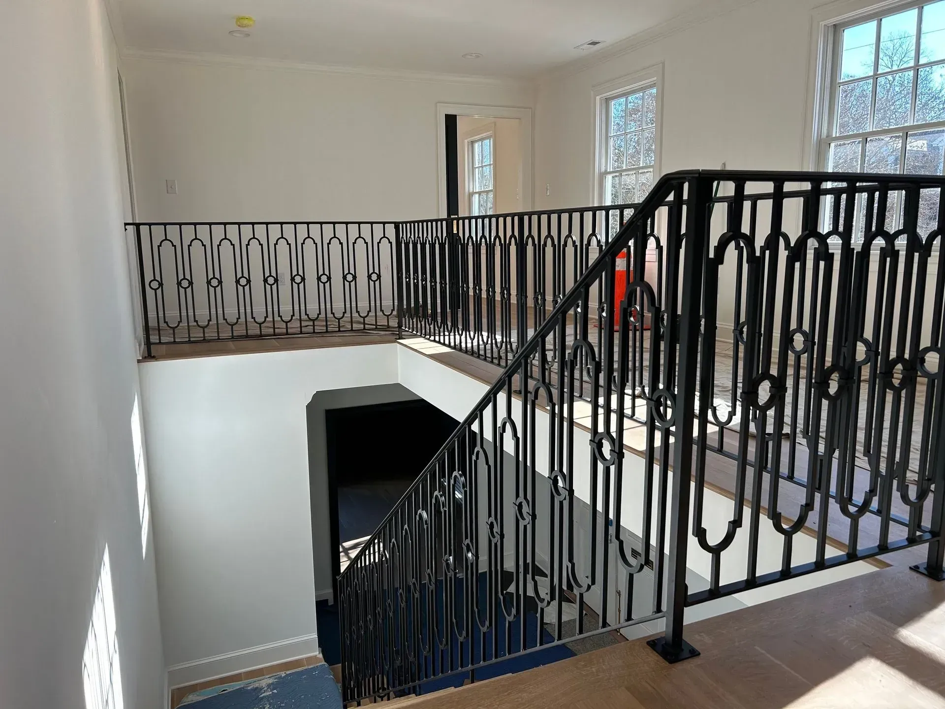Interior view of a home with a black iron railing system around a stairway and loft. Light streams in from the windows.