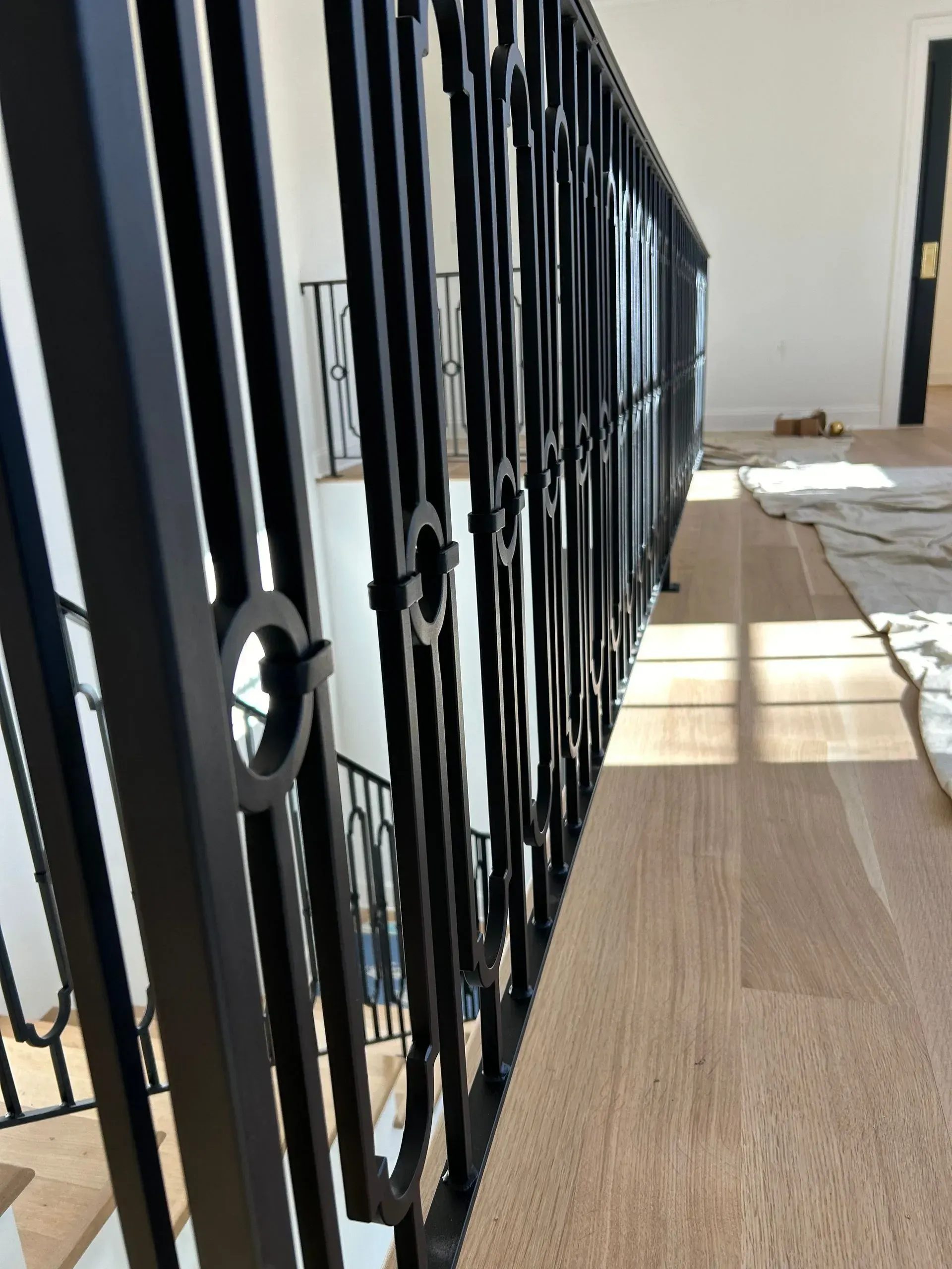 A black metal gate in front of a brick wall and grassy yard, beside a red building on a sunny day.