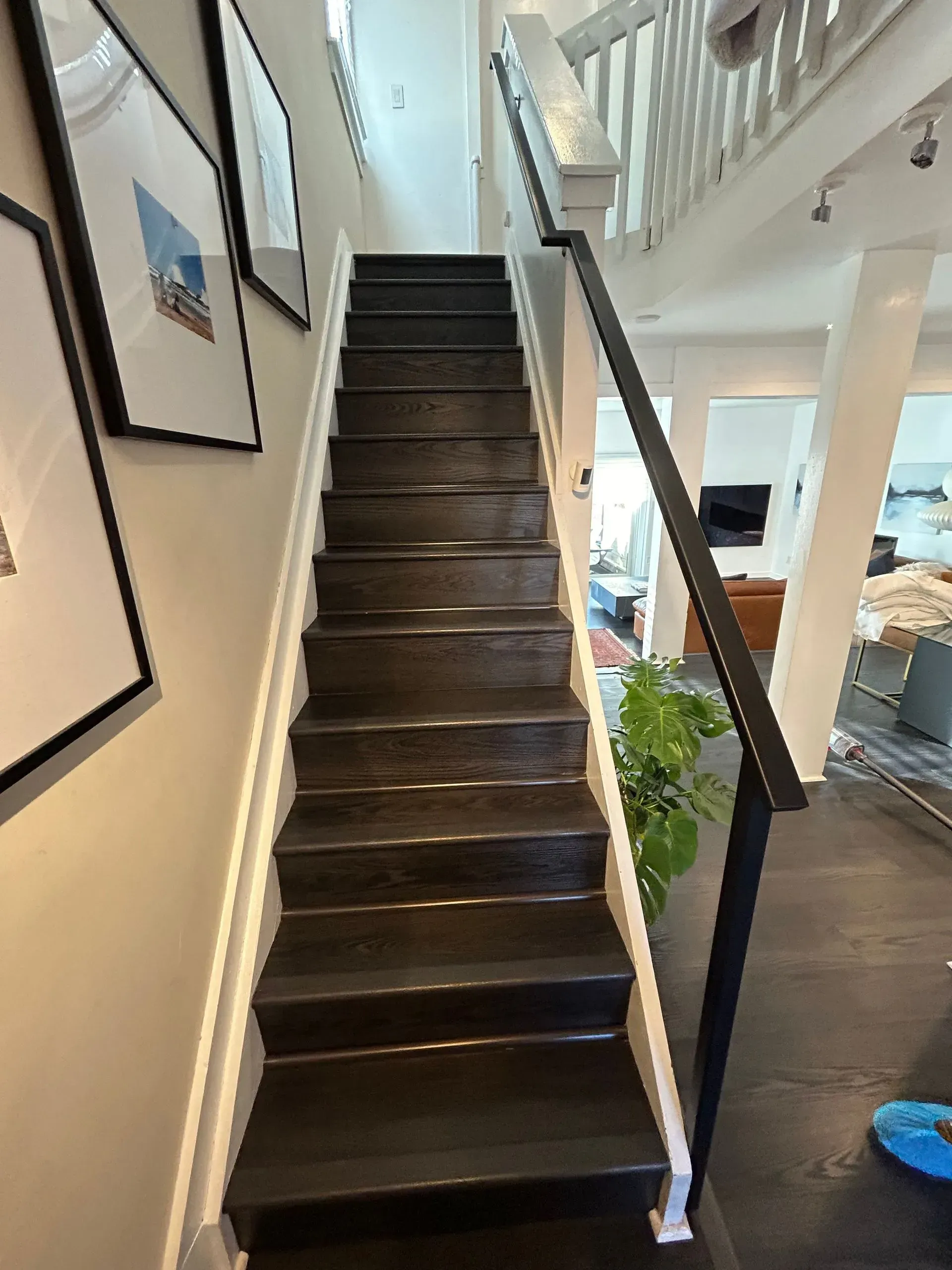 Dark wooden staircase with white trim. Black metal railing on the right, framed art on the left.
