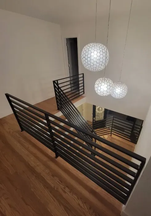 Overhead view of a modern staircase with black horizontal railings, hardwood floors, and three hanging white orb lights.