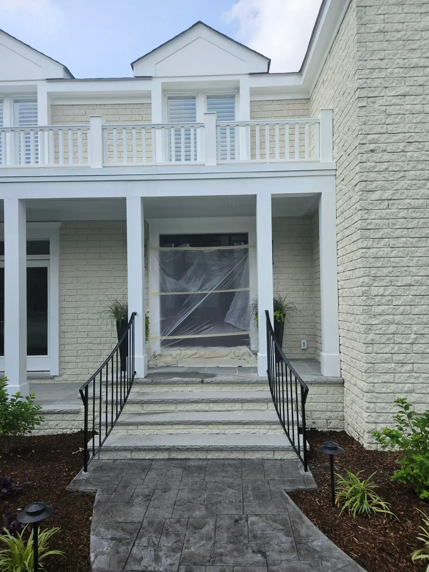 Exterior view of a light-colored house with a stone facade, entryway with steps and black railings.